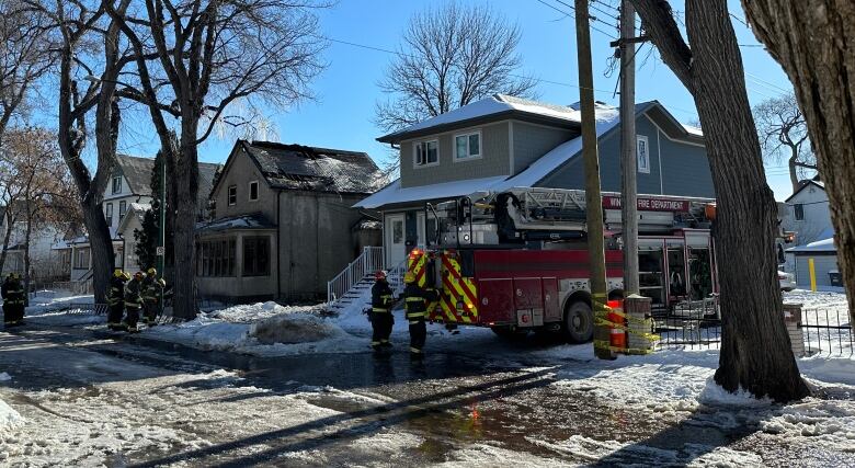 Two firefighters and a fire truck are in front of a house on a residential street.