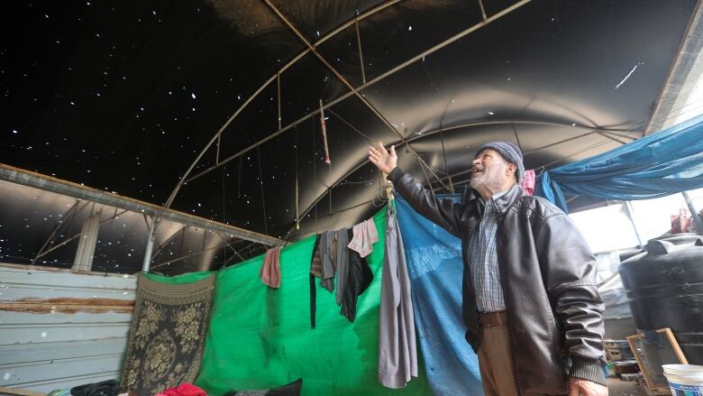 A man stands with his arm raised inside a tent shelter. 