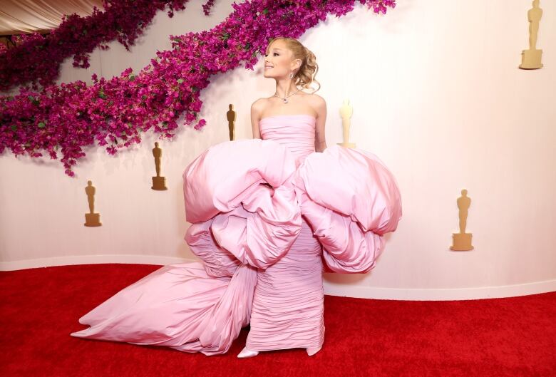 A blond woman wears a large pink dress that puffs at the waist.