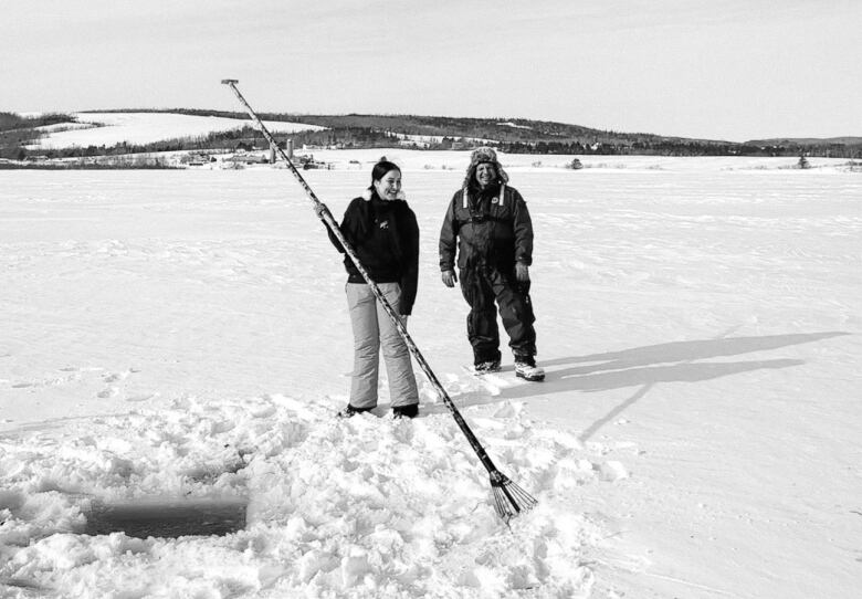 man and woman standing on ice by hole with a spear