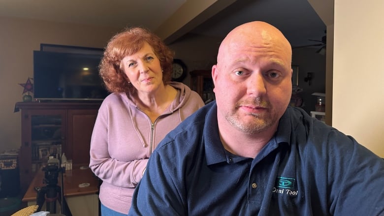 A man sits down and his mom stands behind him.