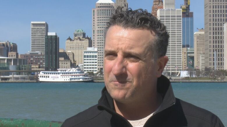 A man stands in front of the Detroit skyline