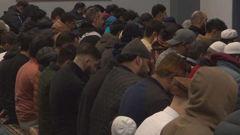 A large group of men are pictured kneeling in a mosque to pray.