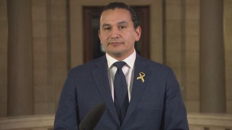 A man in a navy blue suit and tie is pictured looking forward.