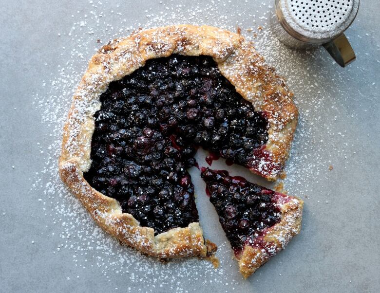 a pie is pictured on a flat marble surface. icing sugar dusts the pie and the counter top.