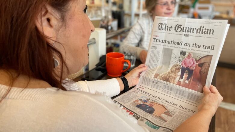 A woman reads the front page of a newspaper.