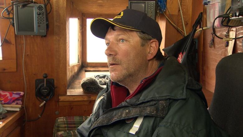 A man wearing a cap sits in the cockpit of a fishing boat. 