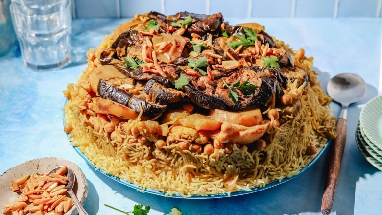 Maqluba (a rice dish with layers of eggplant, chickpeas and cauliflower on top) on a blue serving platter on a blue countertop. 