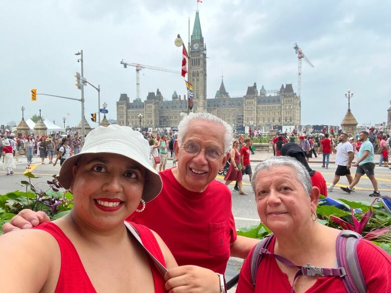 A family dressed all in red poses for a selfie in front of parliament, with celebration going on in the background.