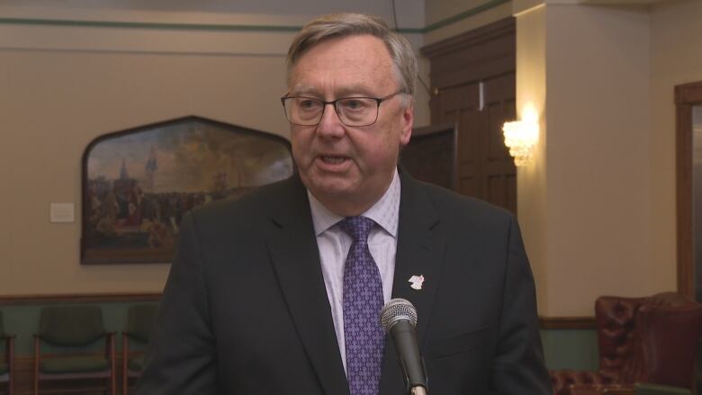 Man in black suit wearing glasses talking into a microphone.