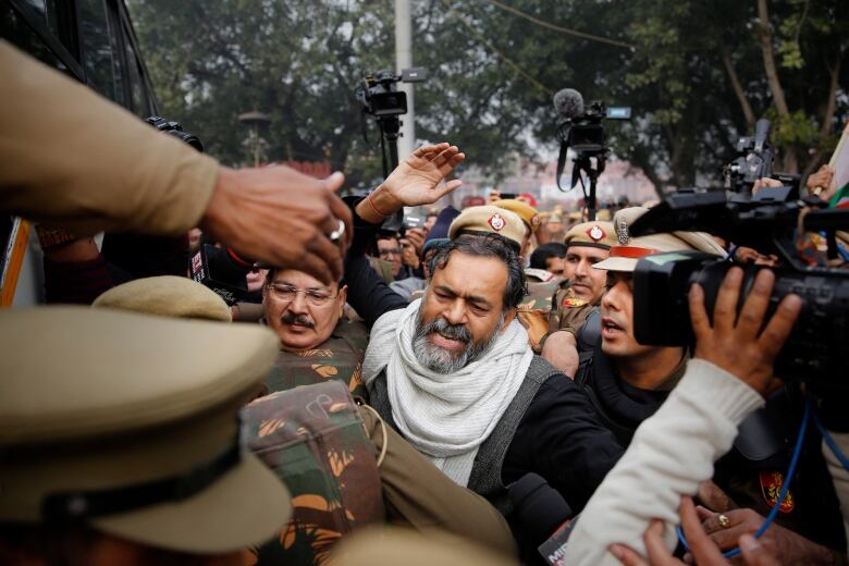 A gray-haired man surrounded on all sides by soldiers and reporters. 