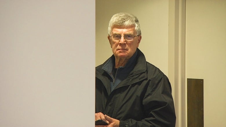 Man with grey hair standing behind wall.