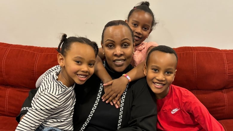 A woman sits with three elementary school-aged children and a rich red-coloured couch.