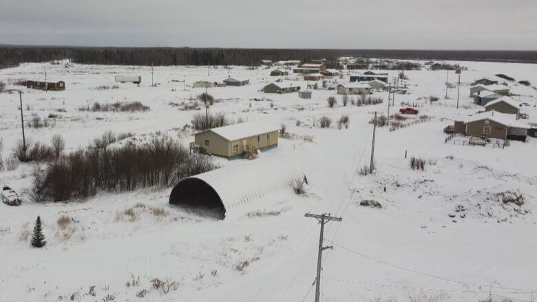 An aerial image from a drone shows homes spaced out in a snow-covered community with dense forest in the background.