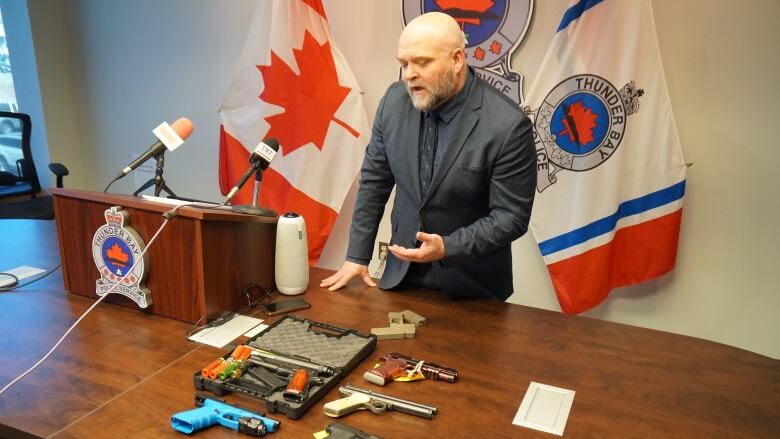 A man speaks with replica handguns laid out on a table in front of him. 