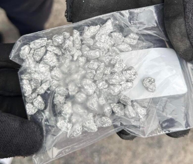 Several small tinfoil balls rolled up in a clear plastic bag are pictured while they're being held in a person's gloved hand.