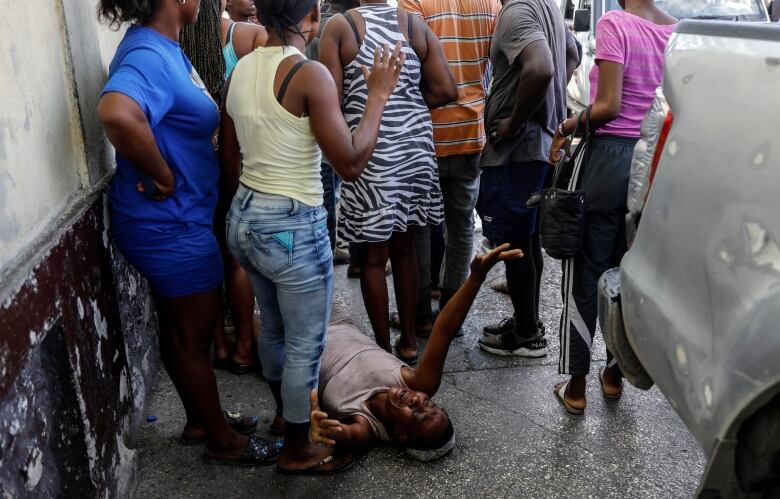 A woman lies on the street mourning, surrounded by a group of other people.