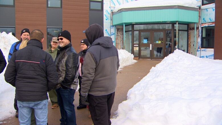 A group of people standing near snowbanks outside of a brick building. 