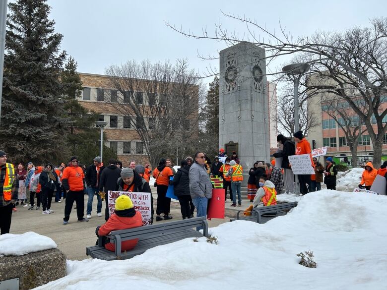 A collection of people, many in orange shirts, gather in front of Saskatoon city hall.