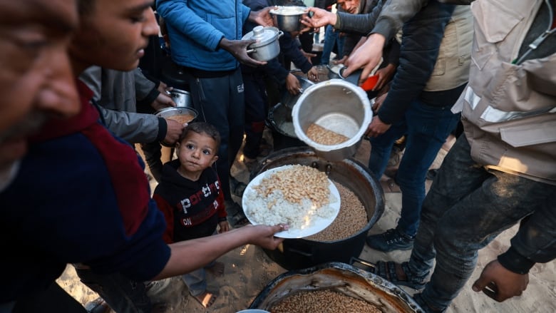 People hold plates and bowls out to receive food. 