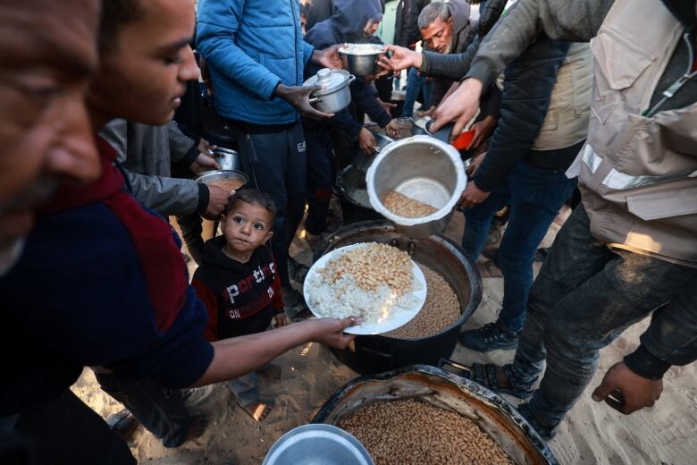 People hold plates and bowls out to receive food. 