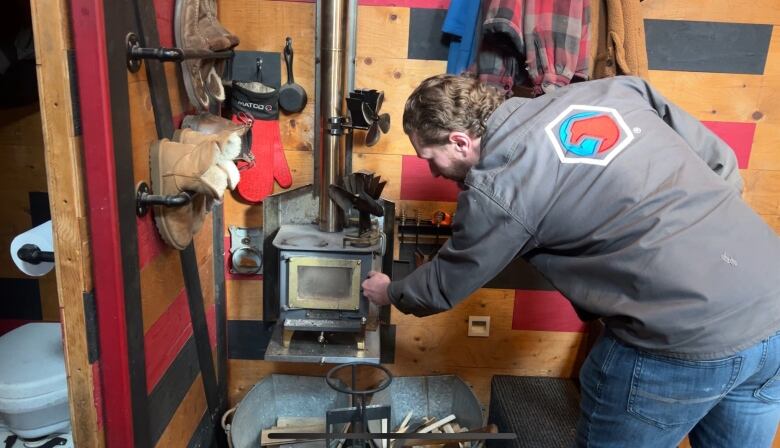 Man is opening a small wood-burning stove in a tiny home. 