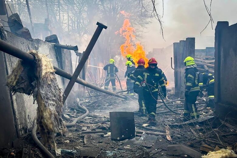 Emergency workers use a firehose amid charred rubble and a fire.