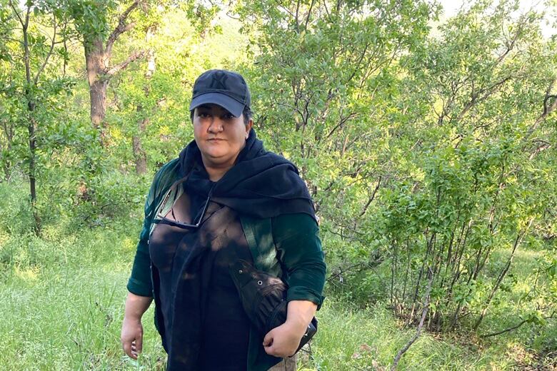 A woman with a baseball cap stands in a forest.