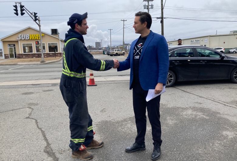 Pierre Polievre shakes hands with a man in workers coveralls 