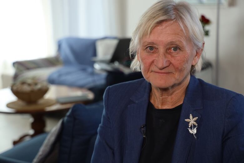 A woman with short white hair and a blue blazer sits in a room.