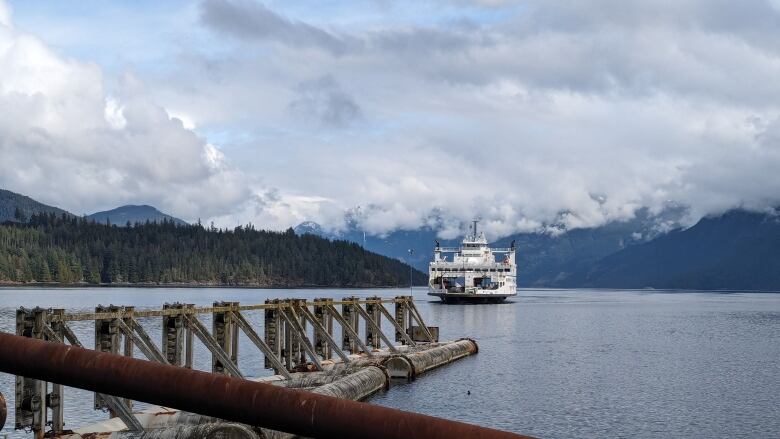 A large white boat is approaching a doc. In the background there are large snow-capped mountains