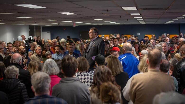 a man with a microphone stands elevated in the middle of a throng of peope.