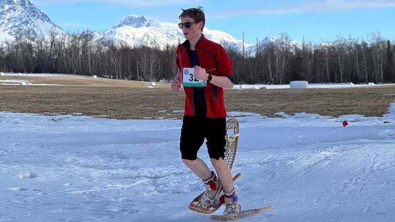 A man snowshoes with grass behind him.