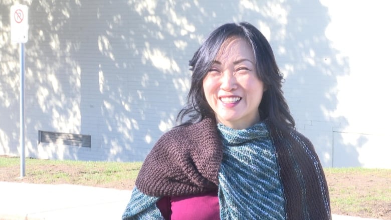 An East Asian woman smiles on a sunny day.