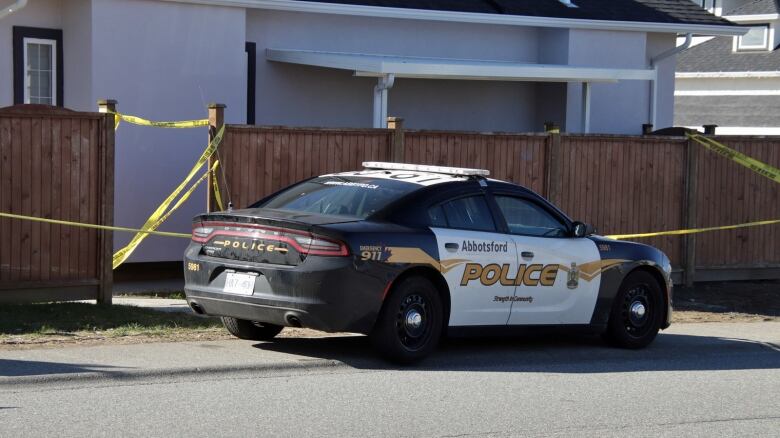 A police car lies parked outside a home surrounded by yellow crime tape.