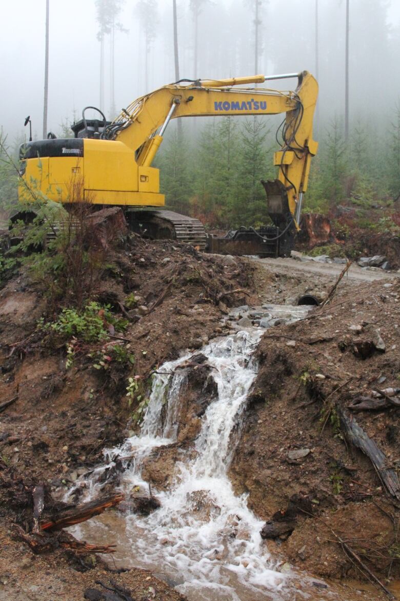 A yellow construction vehicle works near an overflowing culvert.