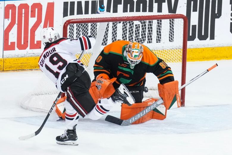 A male ice hockey player wearing number 19 shoots the puck past a goaltender down on one knee during a game.