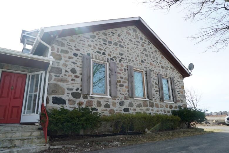 Exterior of a gray rubble stone building with three windows and a red door.