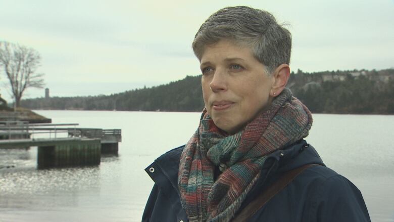 A woman wearing a scarf stands in front of a body of water.