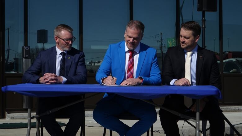 Three men in suits sit at a table.