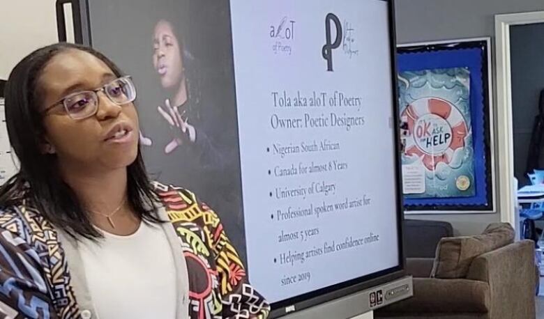 A woman in a colourful sweater stands near a whiteboard.