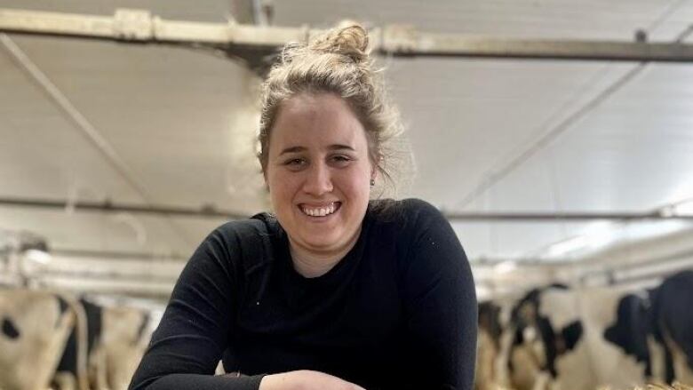 A woman smiling at the camera. Cows are in back of her.