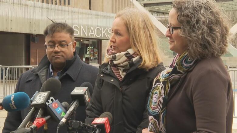 A man and two woman gather to speak around multiple microphones.