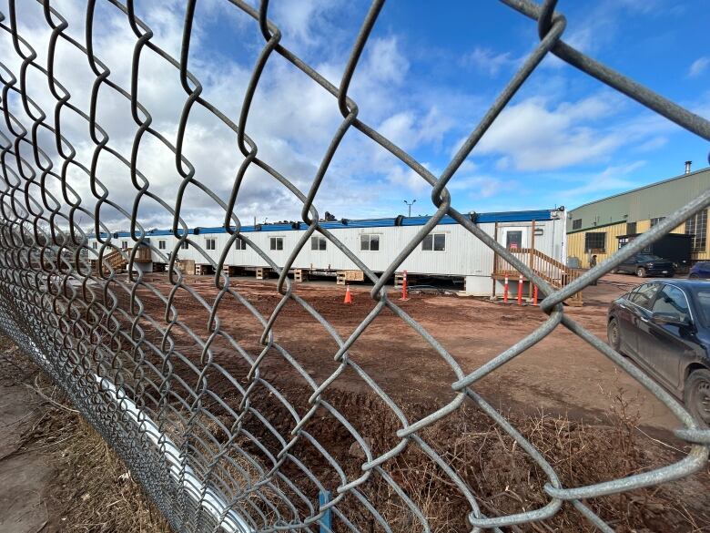 Mobile homes are visible through a gate. THe ground is muddy.