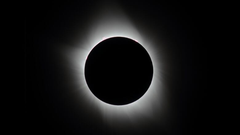 The sky appears black and a white ring is seen around the moon as it blocks out the sun during a total solar eclipse. 