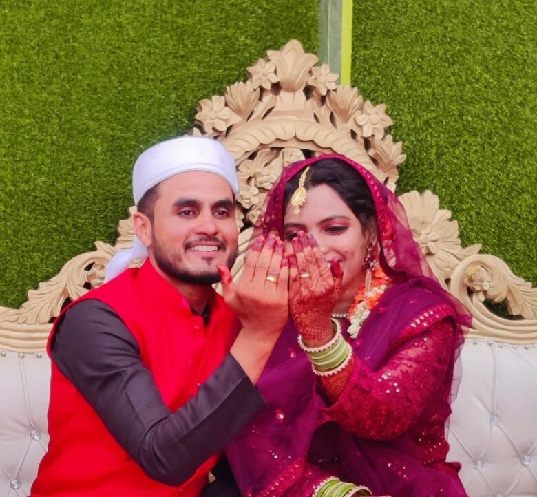 A man and a woman dressed for their wedding hold their hands up, showing their matching rings. 