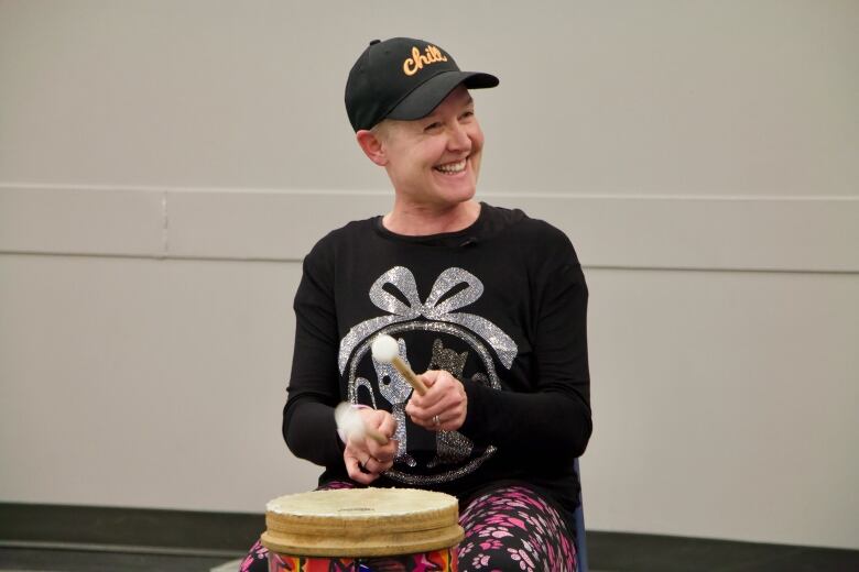 A woman smiles as she plays a drum with two mallets.