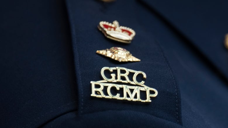 Closeup of a police logo that says GRC RCMP in gold lettering topped with a crown and a pin on a navy blue epaulette.