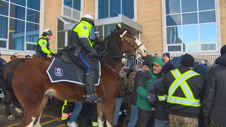 Two police officers in yellow jackets on horses move towards a crowd of people.