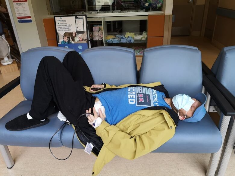 A man lying on a bench of hospital seats.